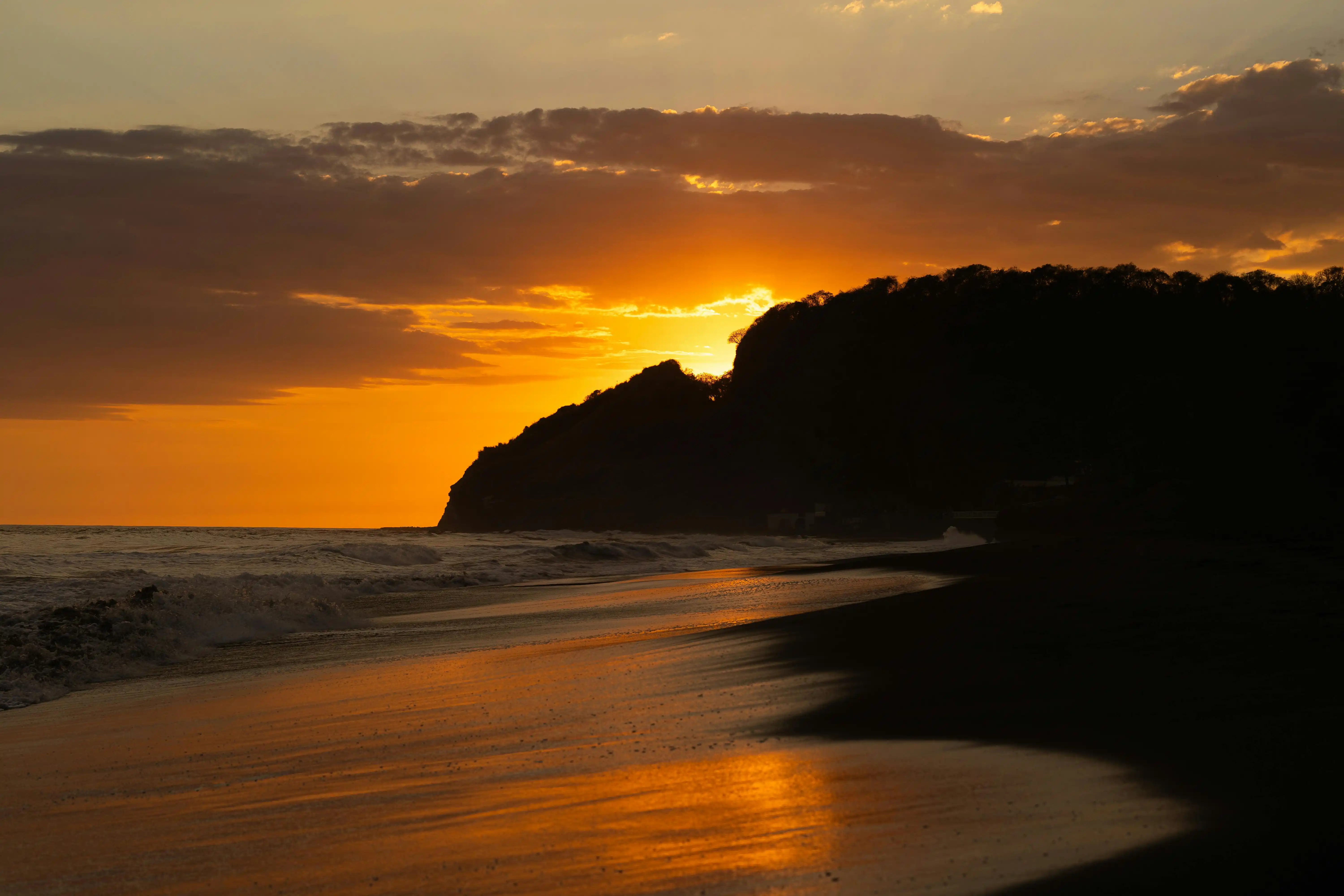 Costa volcánica del Pacífico salvadoreño al atardecer, con olas de surf y playa de arena negra
